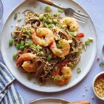 Soba noodles with shrimp on two plates with forks and garnish next to it.