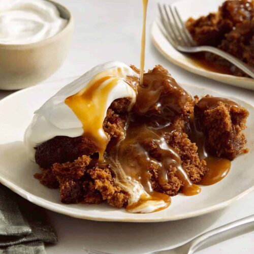 Sticky toffee pudding spooned onto a plate and drizzled with sauce.