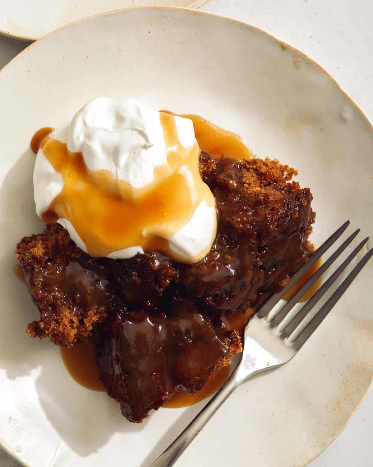 Sticky Toffee pudding on a plate with whipped cream and a fork.