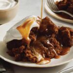 Sticky toffee pudding spooned onto a plate and drizzled with sauce.