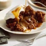 Sticky toffee pudding spooned onto a plate and drizzled with sauce.