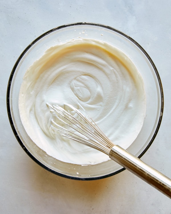 Whipped cream in a glass bowl with a whisk for sticky toffee pudding.