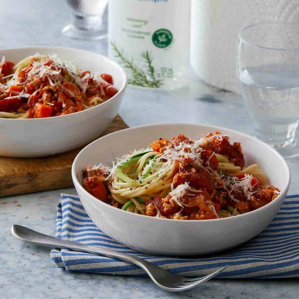 Home Made Simple cleanser next to bowls of turkey bolognese with spaghetti and zucchini noodles.