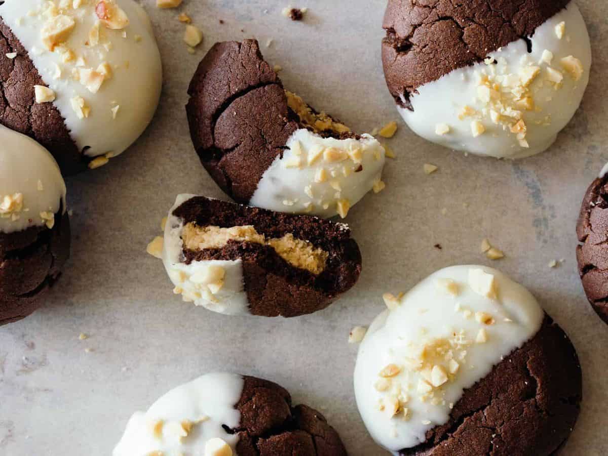 A close up of white chocolate dipped, peanut butter stuffed chocolate cookies, one broken in half.