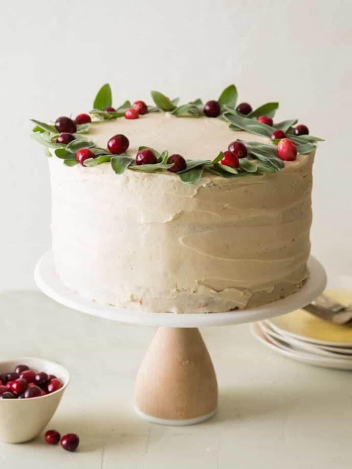 Apple cranberry cake with brown sugar buttercream decorated with fresh cranberries with plates and forks.