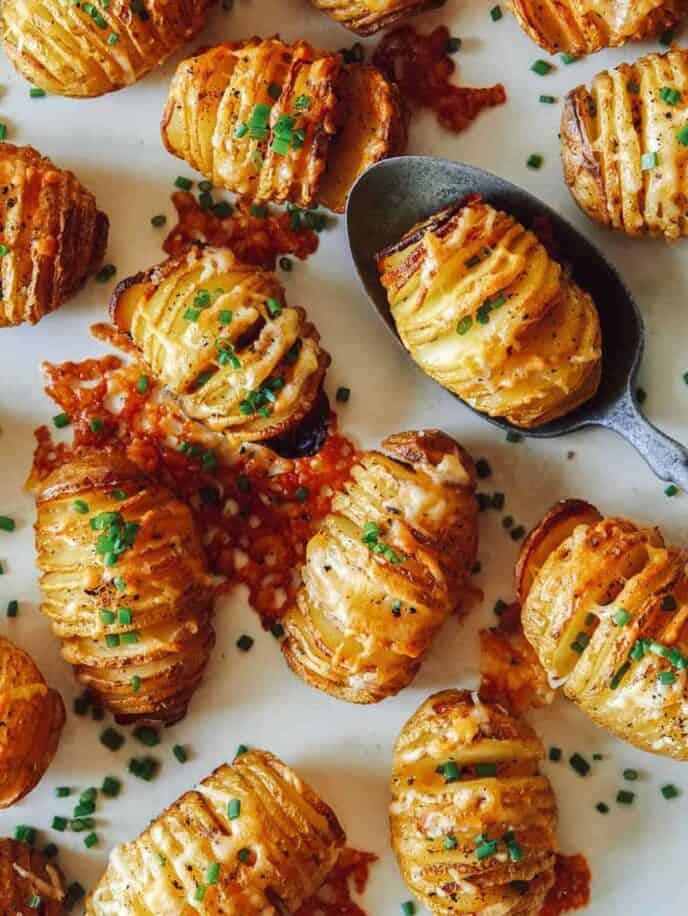 Cheesy Hasselback potatoes on a platter with a spoon.