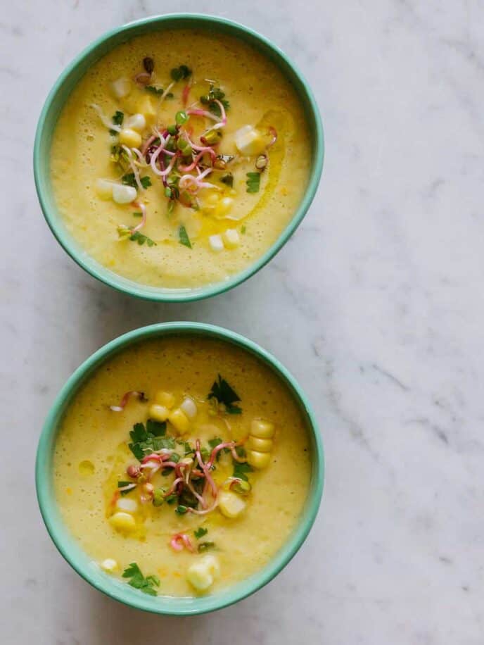 Sweet corn gazpacho in green bowls on a marble surface.