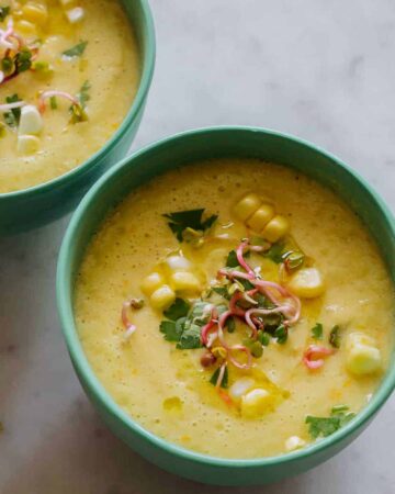A close up of bowls of sweet corn gazpacho with spoons.