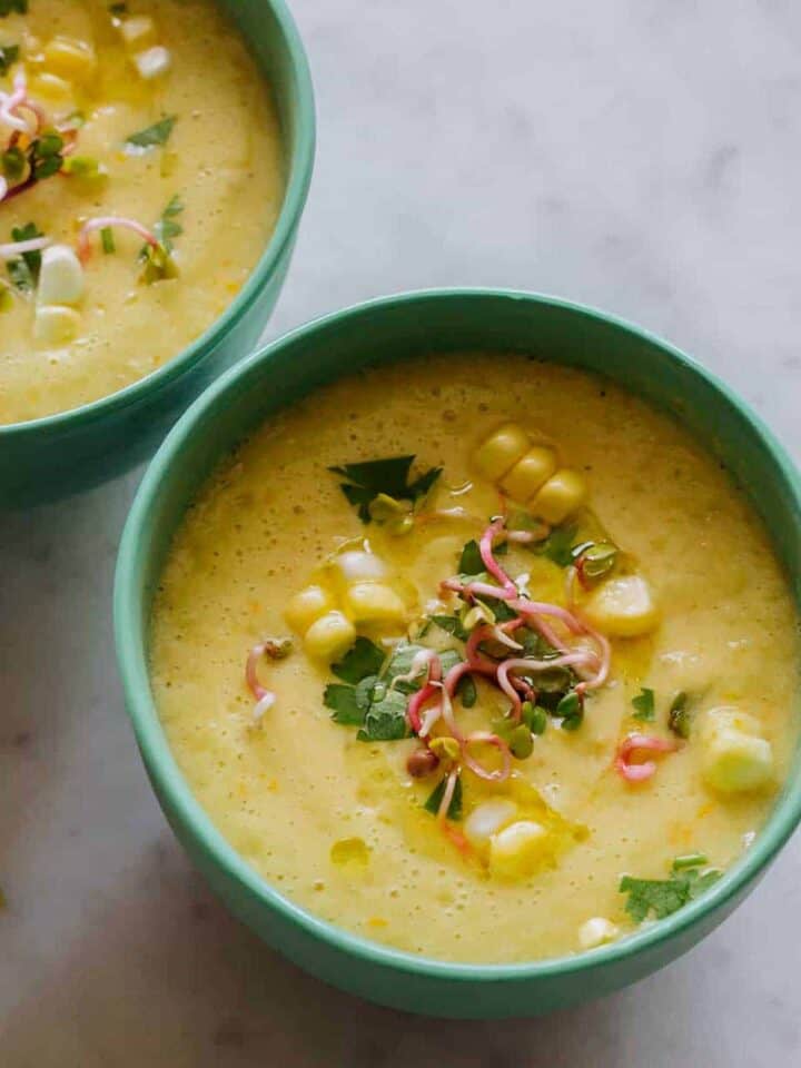 A close up of bowls of sweet corn gazpacho with spoons.