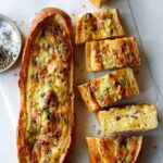 Two baked egg boats on a surface and one cut up.