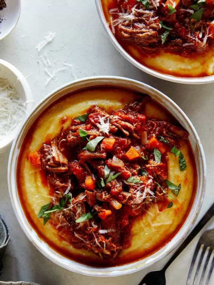 Beef ragu in a bowl with polenta and pepper on the side.