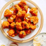 Buffalo cauliflower recipe on a plate with beers next to it.