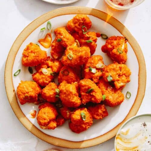 Buffalo cauliflower recipe on a plate with beers next to it.