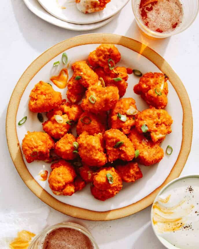 Buffalo cauliflower recipe on a plate with beers next to it.