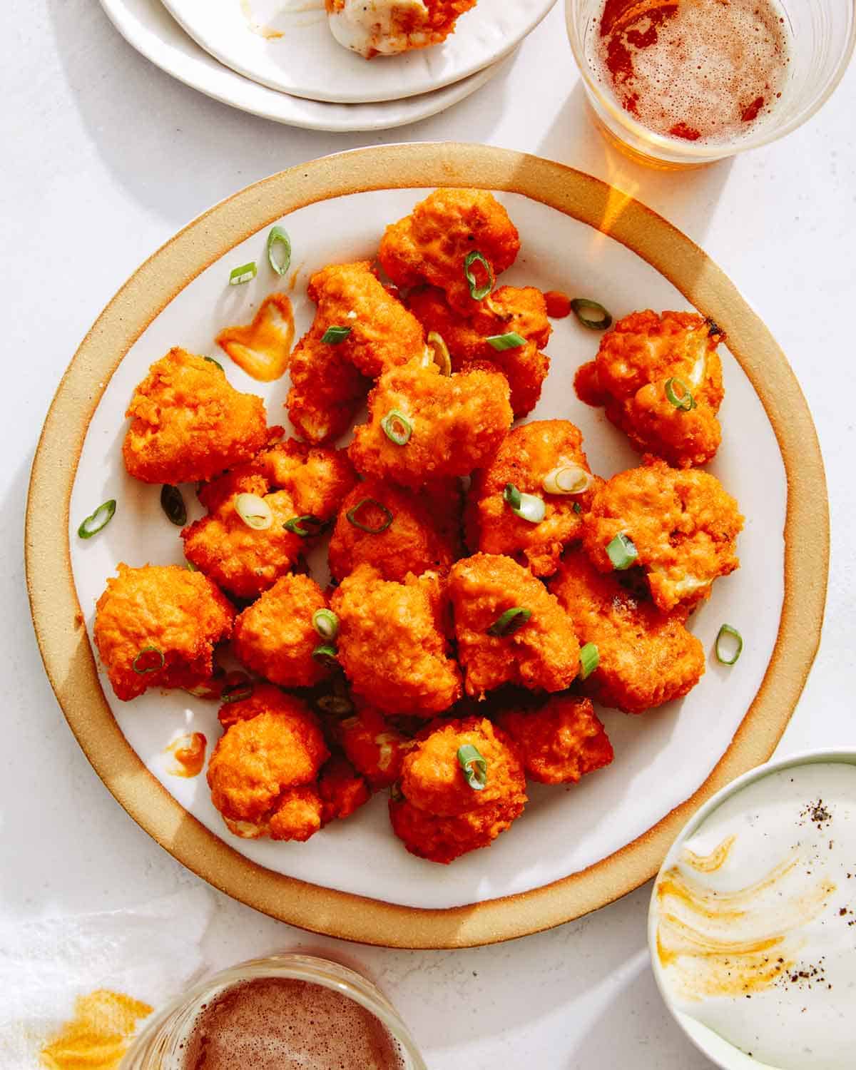 Buffalo cauliflower recipe on a plate with beers next to it, a Super Bowl finger food idea. 
