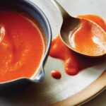 Homemade buffalo sauce in a bowl with a spoon in it.