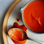 Buffalo sauce in a bowl on a plate with a spoon.