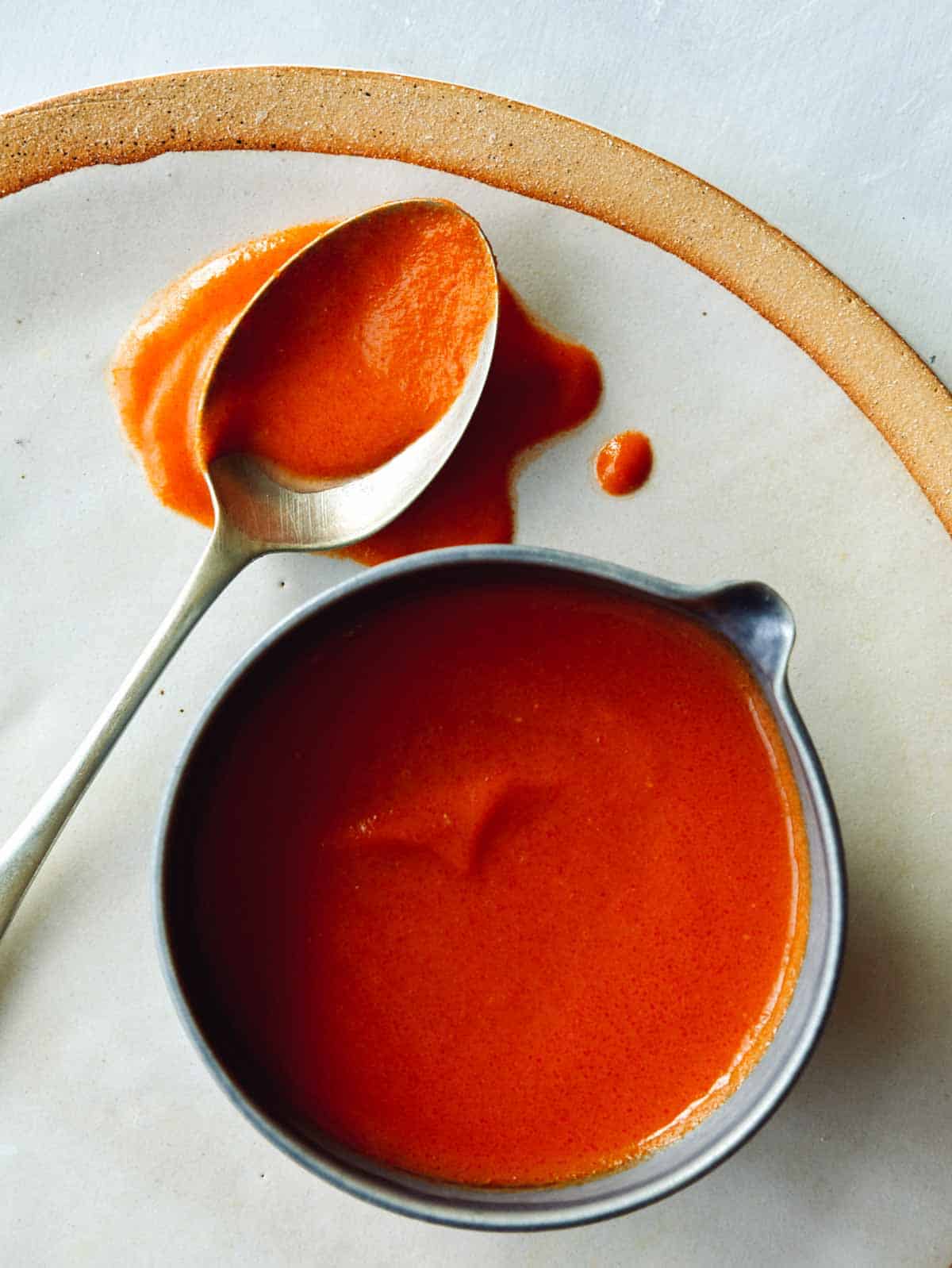 Homemade buffalo sauce in a bowl with a  spoon next to it.  