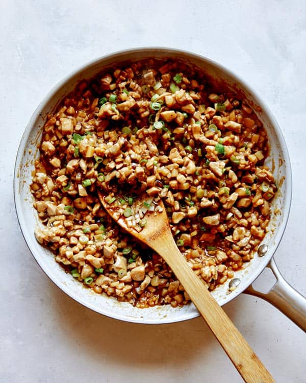 Chicken lettuce wraps in a skillet with green onions.