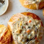 Clam chowder in a bread bowl with a spoon in it.