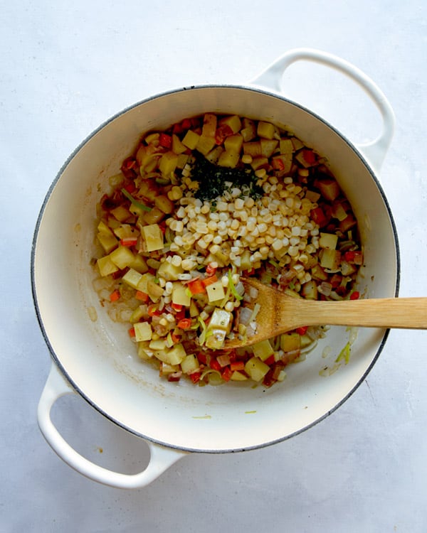 Clam chowder ingredients with corn and thyme added to a pot.
