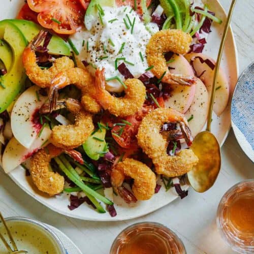 Fried coconut shrimp on top of a bed of lettuce and seasonal summer ingredients.