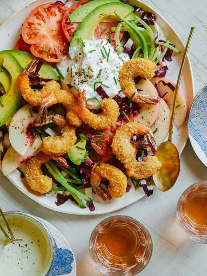 Fried coconut shrimp on top of a bed of lettuce and seasonal summer ingredients.