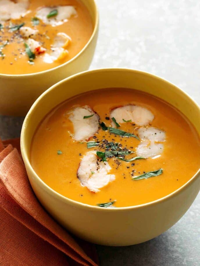 A close up of bowls of lobster bisque garnished with pieces of lobster meat and tarragon.