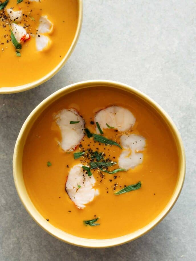 Two bowls of lobster bisque on a surface.