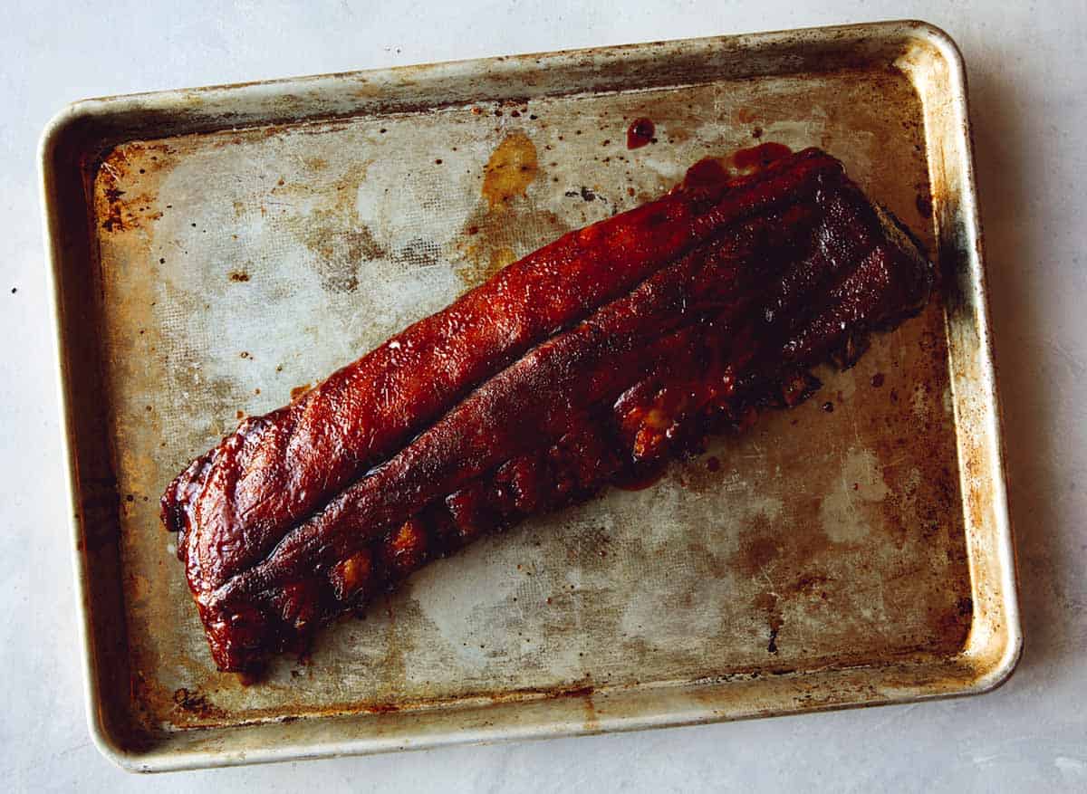 Sticky oven baked ribs on a a baking sheet ready to be cut up.