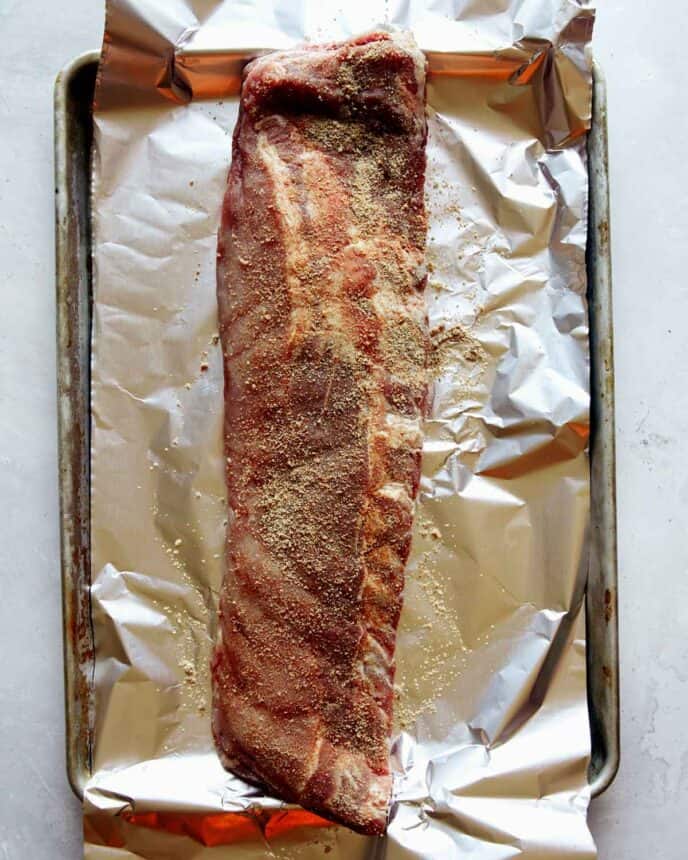 Ribs rubbed with spice on baking sheet with tin foil.