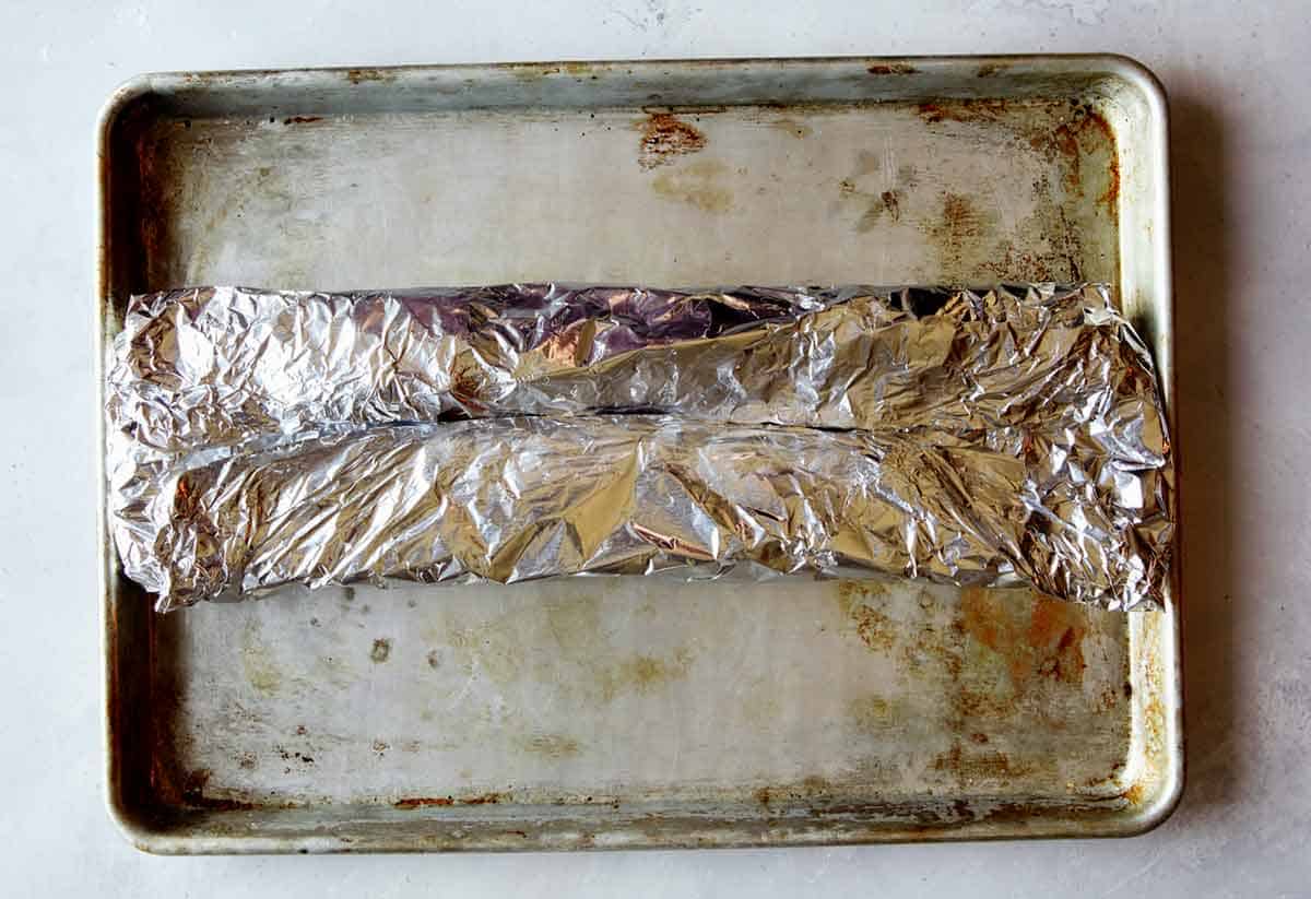 Ribs wrapped in tin foil on a baking sheet to make oven baked ribs.
