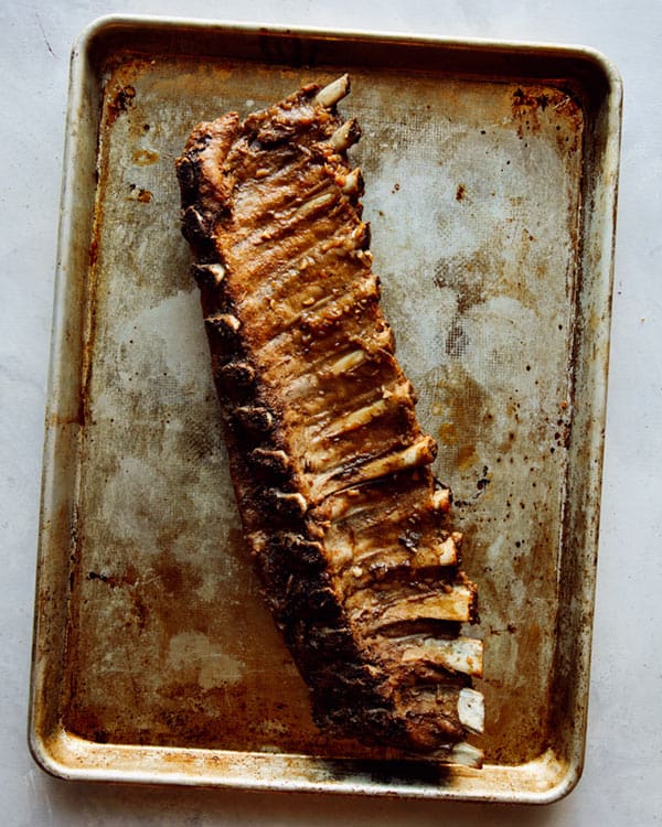 Oven baked ribs on a baking sheet ready to have sauce brushed on top.