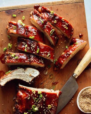 Sticky oven baked ribs being cut on a cutting board.