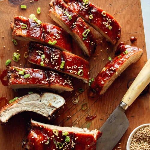 Sticky oven baked ribs being cut on a cutting board.