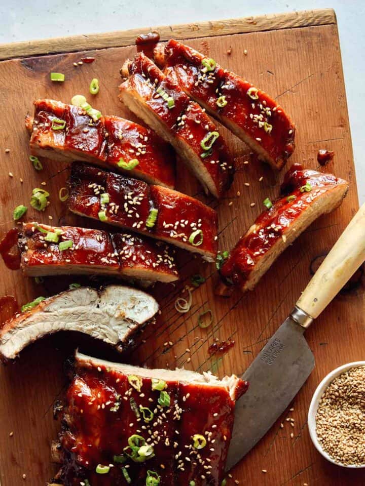 Sticky oven baked ribs being cut on a cutting board.