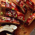 Oven baked sticky ribs with sesame seeds and green onions on a cutting board.