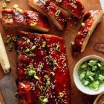 Oven baked ribs with sesame seeds and green onions on a cutting board.