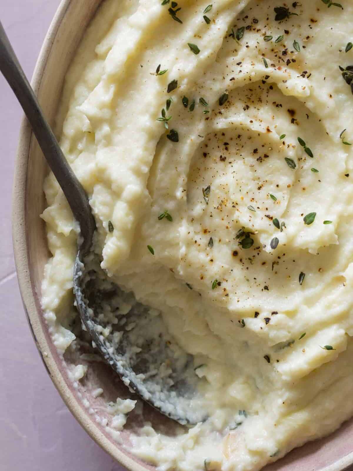 A close up of parsnip, cauliflower, and roasted garlic mash with a spoon.