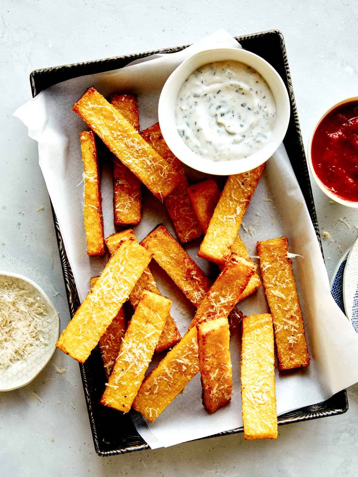 Polenta fries in a basket with dipping sauces next to it.