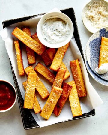 Polenta fries in a basket with dipping sauces next to it.