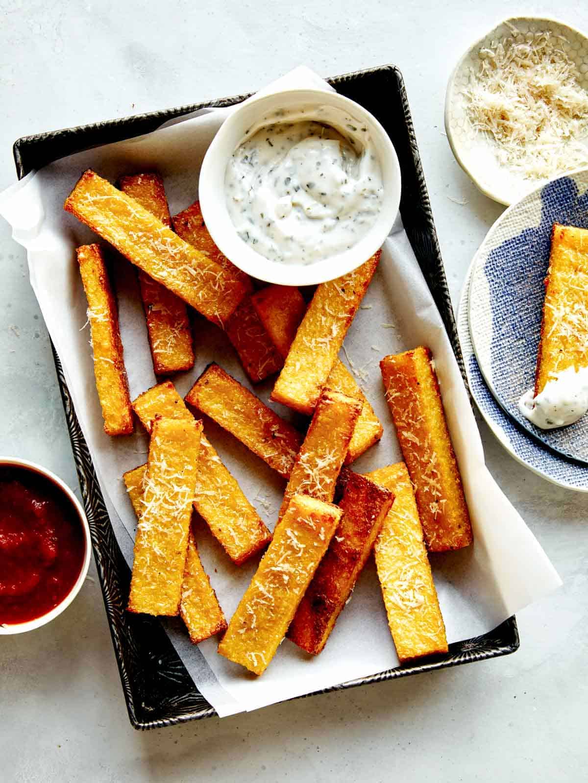 Polenta fries in a basket with dipping sauces next to it. 