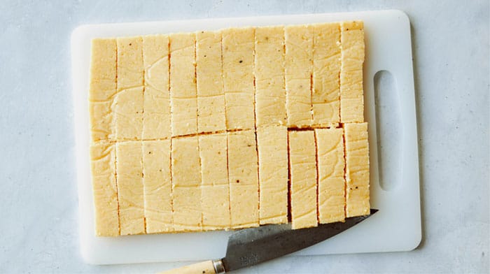 Cooled polenta cut into sticks on a cutting board.