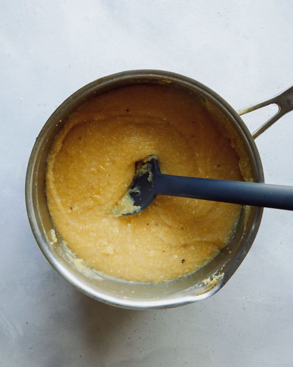 Polenta in a pot mixed with butter and cheese.