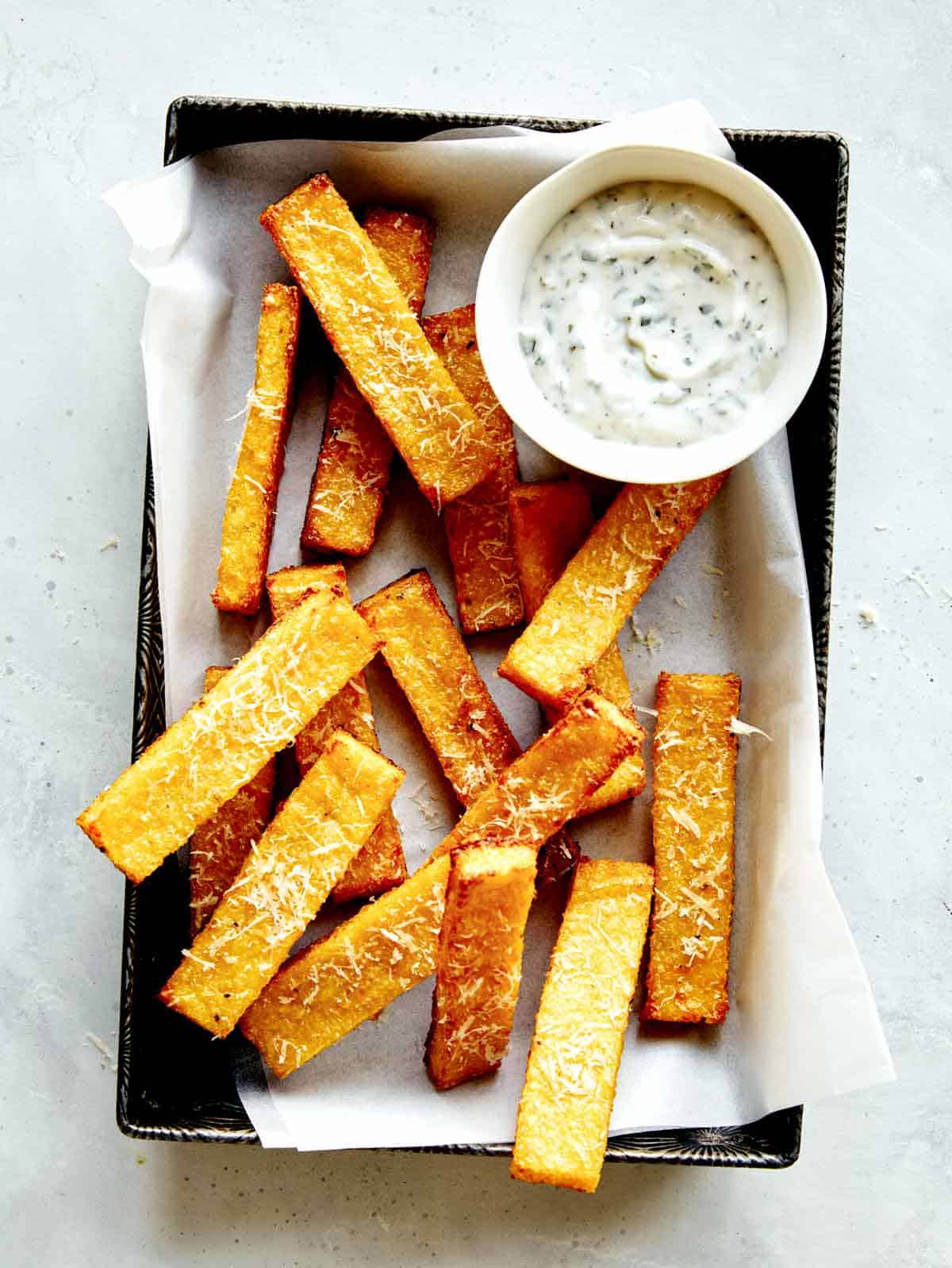 Polenta fries in a basket with dipping sauces next to it.