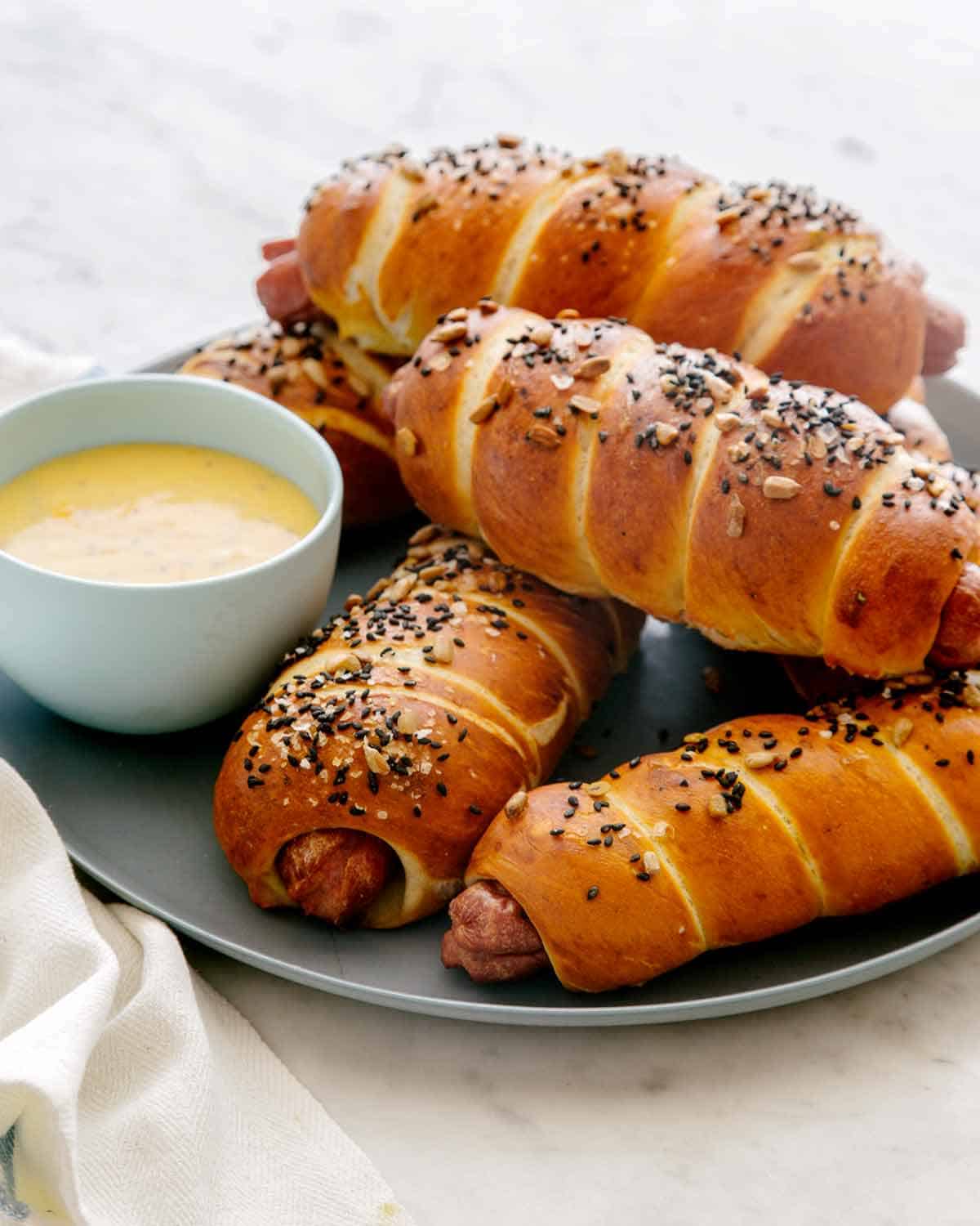 Pretzel dogs with a side of cheese sauce on a blue plate.