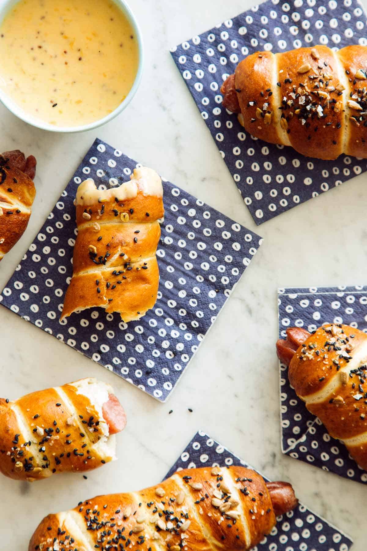 Half eaten pretzel dogs with a side of cheese sauce on blue napkins.