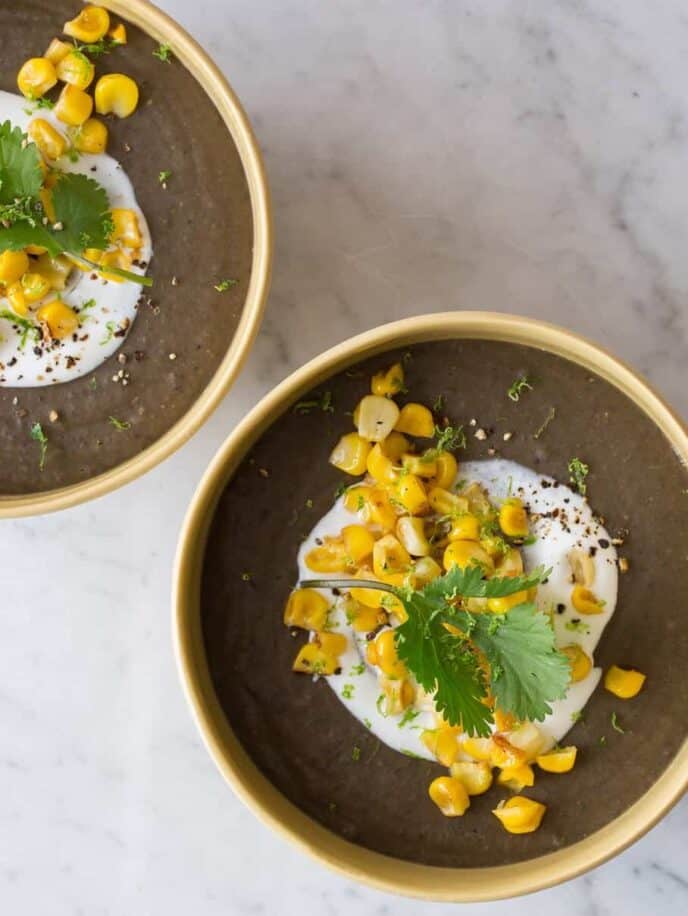 Bowls of spicy black bean soup garnished with sour cream, roasted corn, and cilantro.