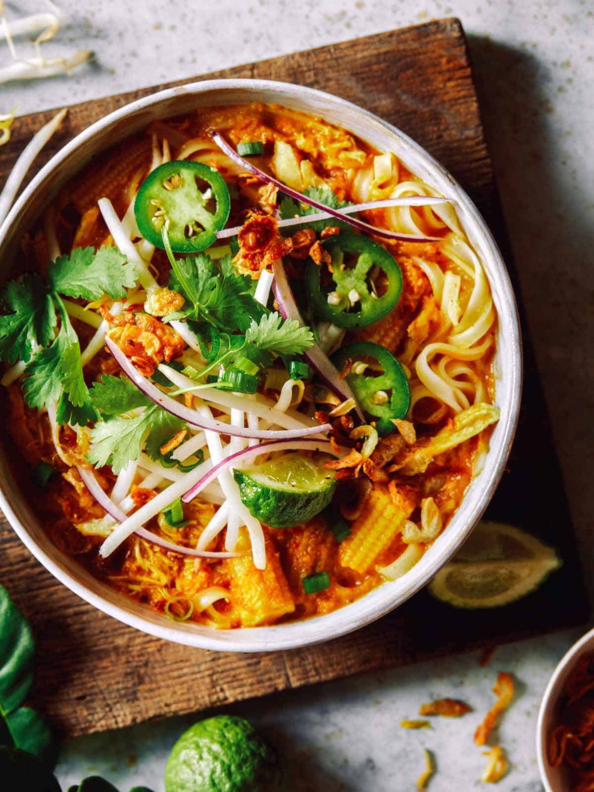 Spicy chicken laksa in a bowl on a cutting board. 