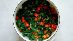 Kale, sweet potatoes, and onions in a stock pot cooking to make tortellini soup.
